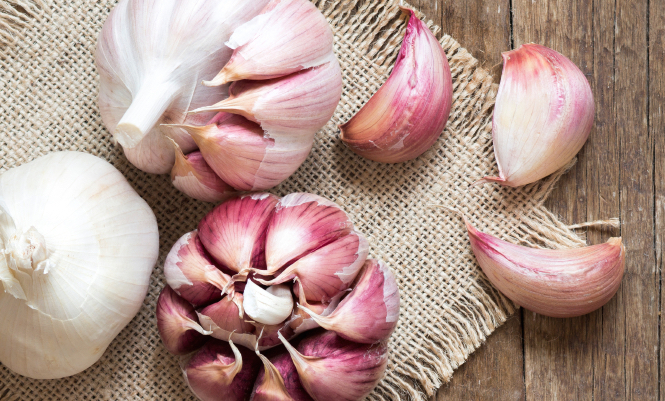 Whole and split fresh garlic on wooden background